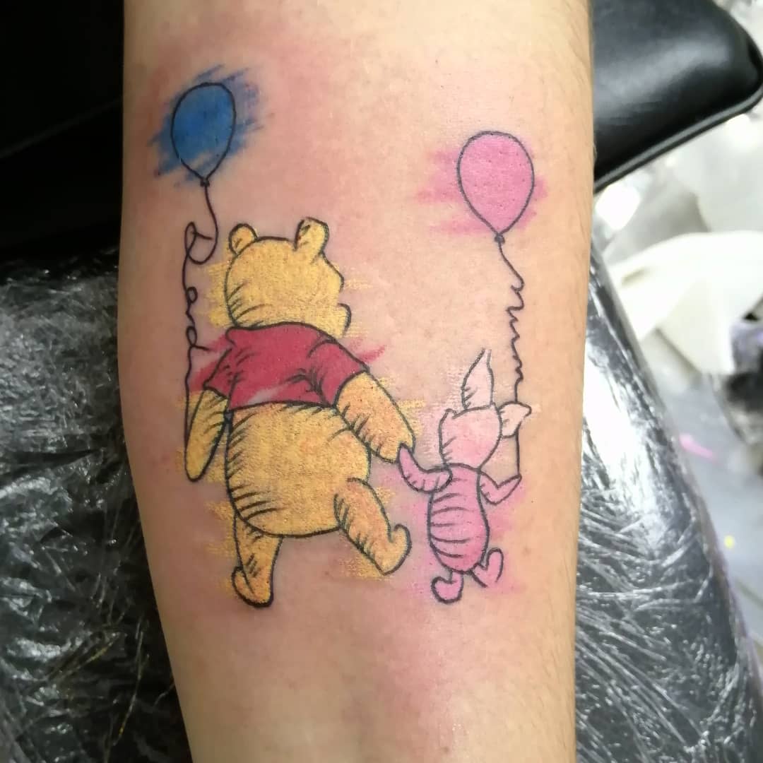 Tattoo of Winnie the Pooh and Piglet holding hands and balloons on an arm
